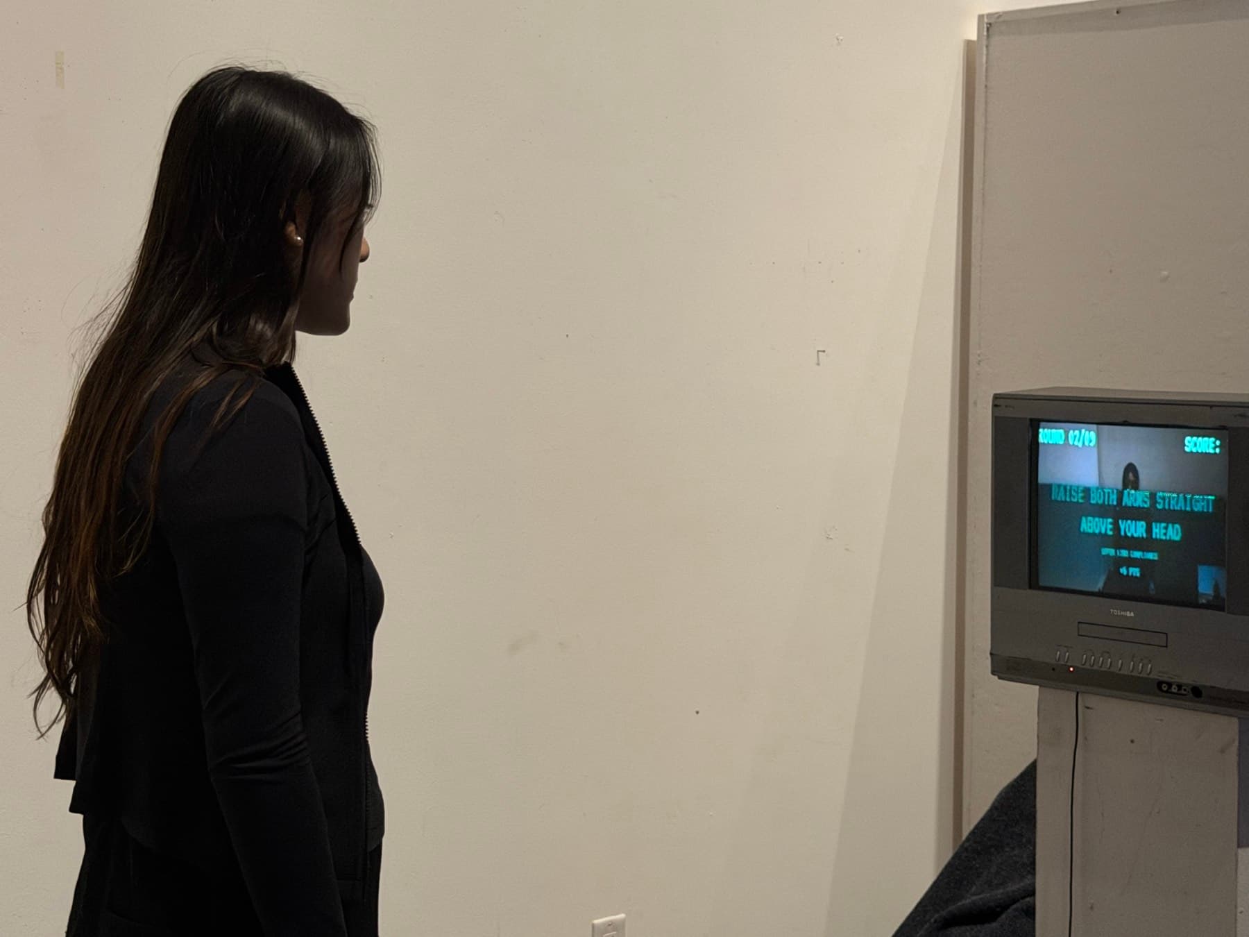 A visitor stands before the CRT as it shows the command 'raise both arms straight above your head'